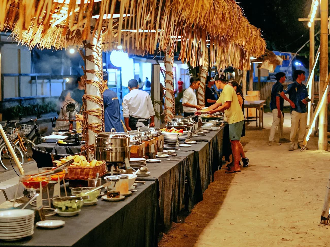 An evening BBQ buffet spread under a thatched beachside roof