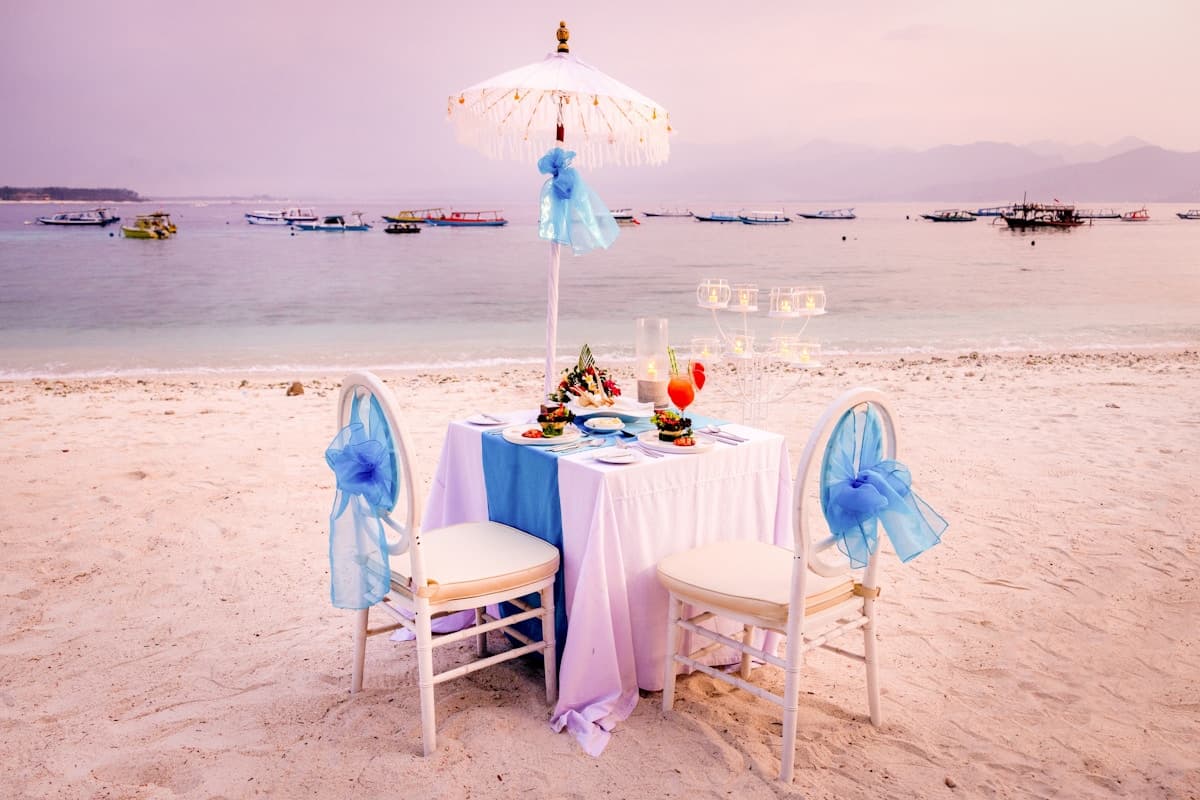 Meja makan romantis di tepi pantai Vila Ombak dihias lilin saat senja